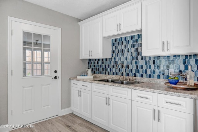 kitchen featuring white cabinetry, backsplash, light hardwood / wood-style floors, and sink