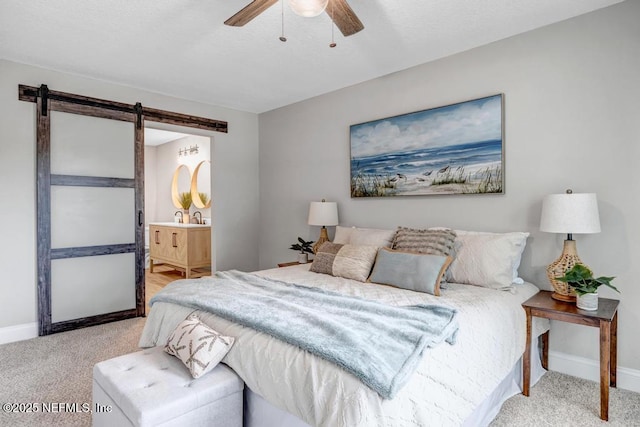 bedroom with ceiling fan, connected bathroom, a barn door, and light carpet