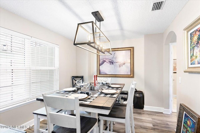 dining room with wood-type flooring, a textured ceiling, and a notable chandelier