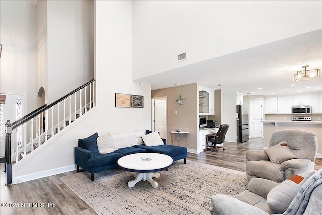 living room with a high ceiling, a textured ceiling, and light wood-type flooring