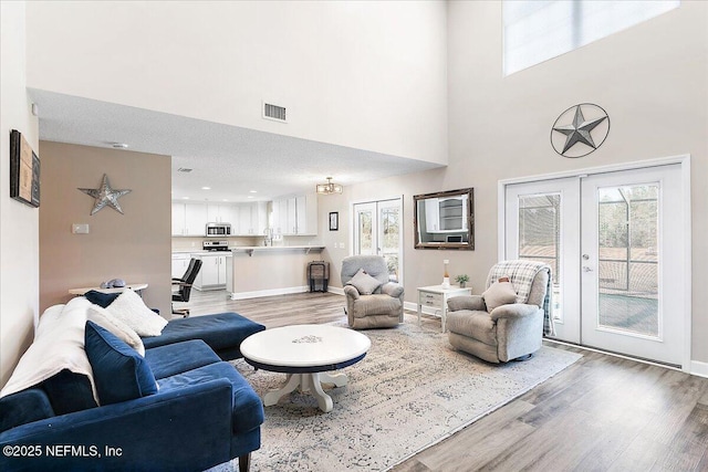 living room featuring a towering ceiling, a wealth of natural light, french doors, and light wood-type flooring