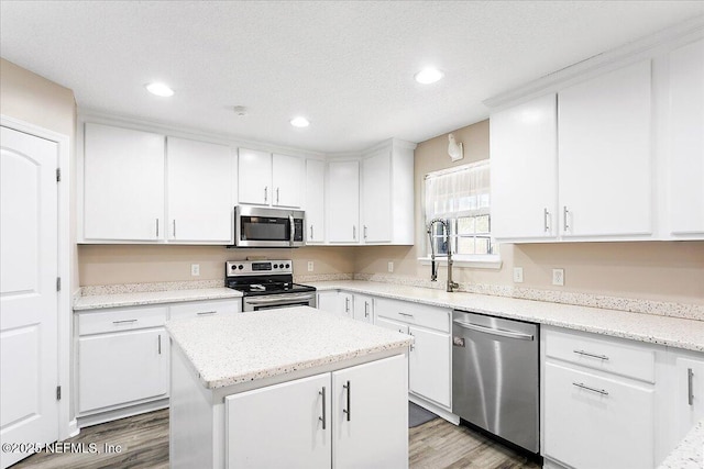 kitchen with white cabinetry, appliances with stainless steel finishes, a center island, and wood-type flooring