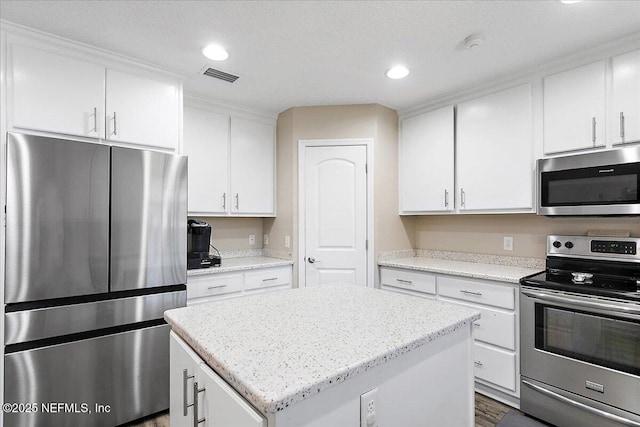 kitchen featuring appliances with stainless steel finishes, white cabinetry, dark hardwood / wood-style floors, light stone counters, and a kitchen island