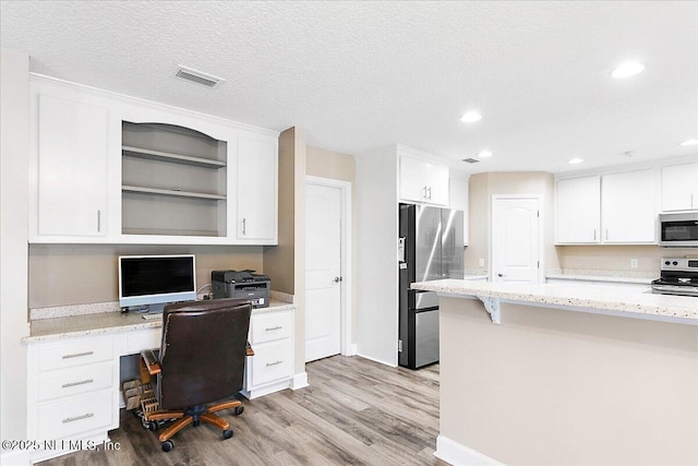 office featuring light wood-type flooring, built in desk, and a textured ceiling