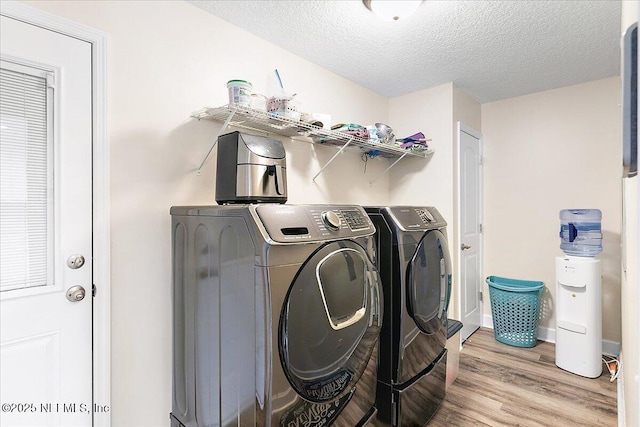 clothes washing area with a textured ceiling, washing machine and clothes dryer, and light wood-type flooring