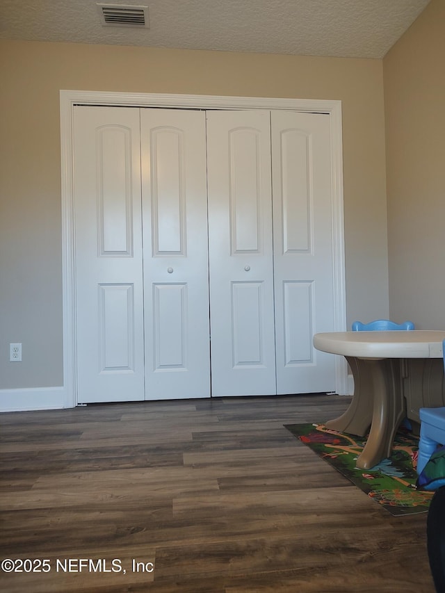 interior space with a textured ceiling, dark hardwood / wood-style flooring, and a closet