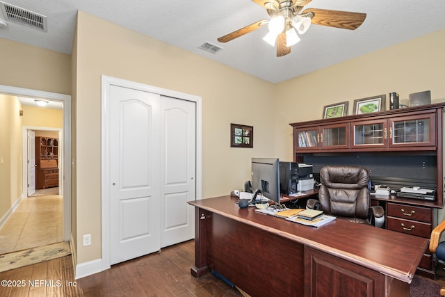 home office featuring a textured ceiling, dark wood finished floors, visible vents, and a ceiling fan