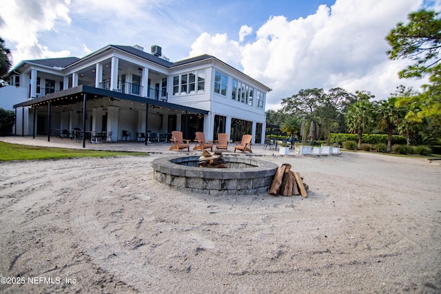 rear view of house with ceiling fan, a fire pit, a patio area, and a balcony