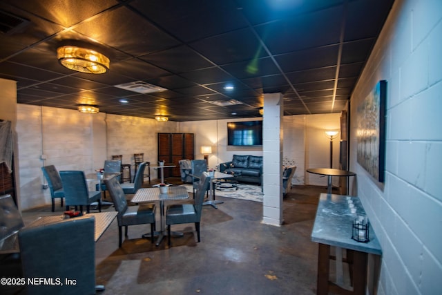 dining area featuring concrete flooring, concrete block wall, visible vents, and a drop ceiling