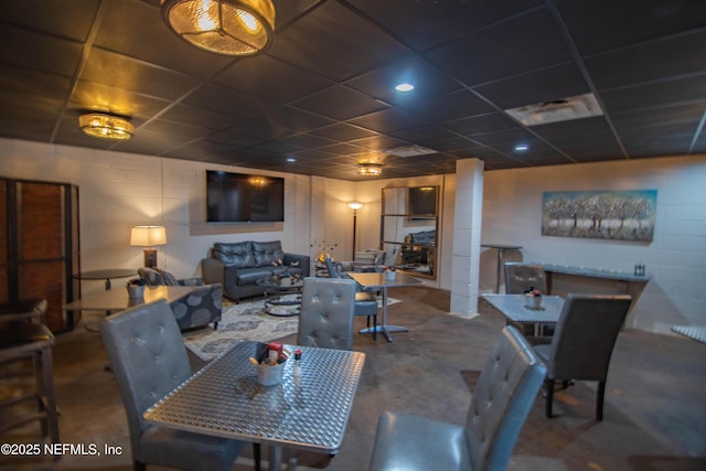 dining area featuring a paneled ceiling, concrete floors, and concrete block wall