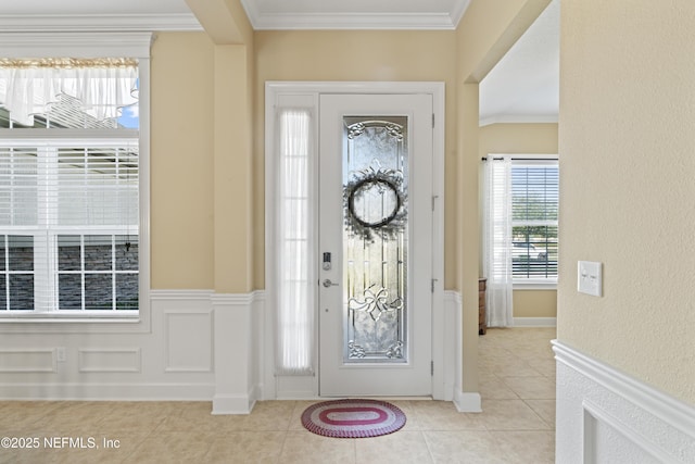 foyer with a wainscoted wall, a decorative wall, light tile patterned flooring, and crown molding