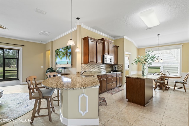 kitchen featuring light tile patterned floors, a sink, visible vents, a center island, and stainless steel microwave