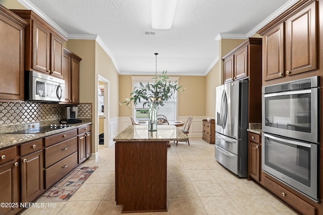 kitchen with light tile patterned floors, a wainscoted wall, stainless steel appliances, visible vents, and a center island