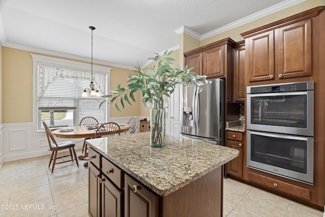 kitchen featuring stainless steel appliances, ornamental molding, a kitchen island, and light stone countertops