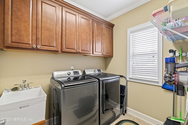 clothes washing area featuring cabinet space, baseboards, crown molding, separate washer and dryer, and a sink