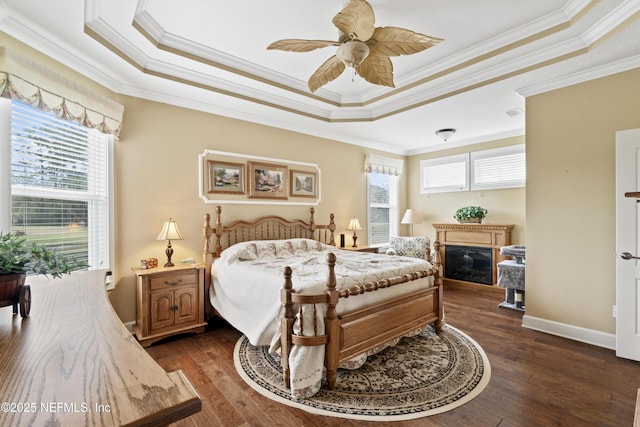 bedroom featuring dark wood-style floors, a tray ceiling, a glass covered fireplace, and crown molding