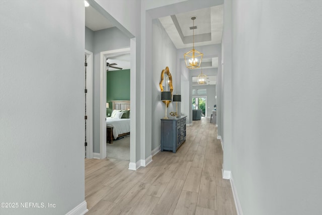 hallway featuring light hardwood / wood-style floors, an inviting chandelier, and a raised ceiling