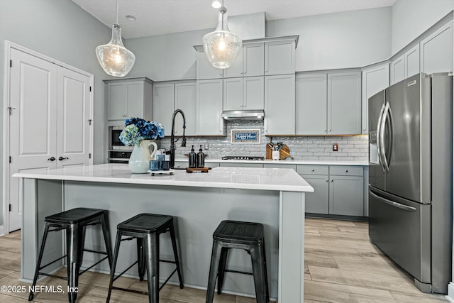 kitchen featuring decorative light fixtures, a kitchen bar, a kitchen island with sink, and appliances with stainless steel finishes