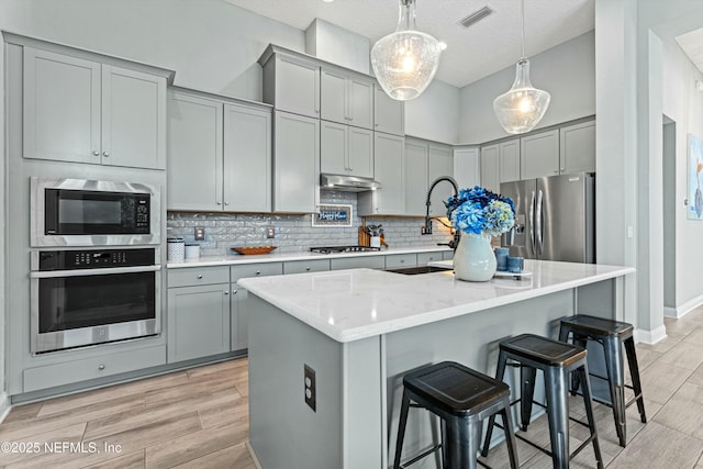 kitchen featuring light stone counters, hanging light fixtures, stainless steel appliances, a center island with sink, and tasteful backsplash