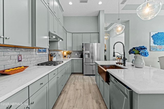 kitchen with a kitchen island with sink, appliances with stainless steel finishes, a textured ceiling, decorative light fixtures, and sink