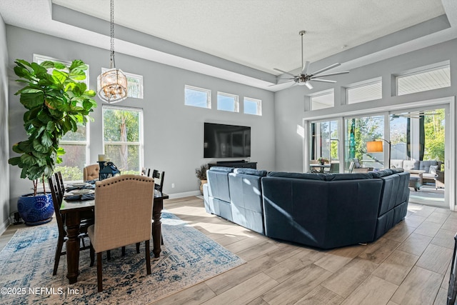 living room featuring ceiling fan with notable chandelier, a textured ceiling, and a tray ceiling