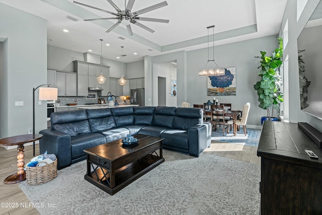 living room featuring light wood-type flooring, ceiling fan, and a tray ceiling