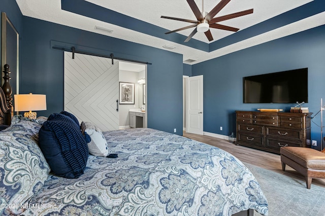 bedroom featuring a barn door, ceiling fan, a textured ceiling, light hardwood / wood-style flooring, and ensuite bathroom