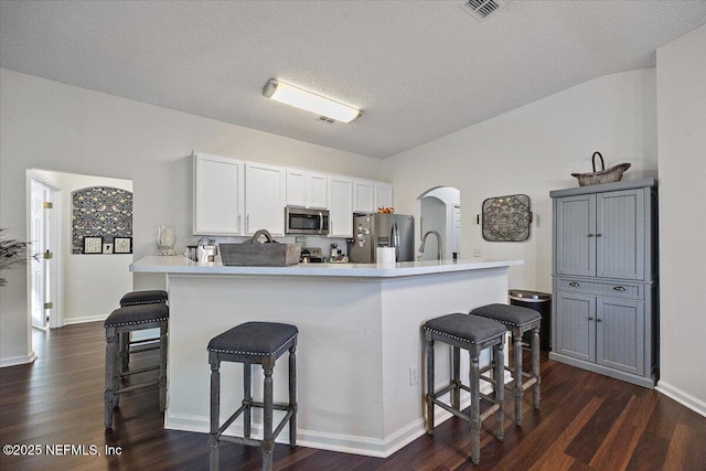 kitchen with a textured ceiling, white cabinets, appliances with stainless steel finishes, a kitchen breakfast bar, and dark hardwood / wood-style floors