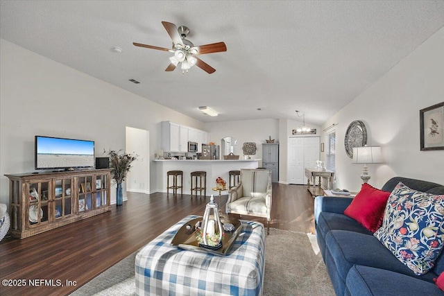 living room with lofted ceiling, dark wood-type flooring, ceiling fan with notable chandelier, and a textured ceiling