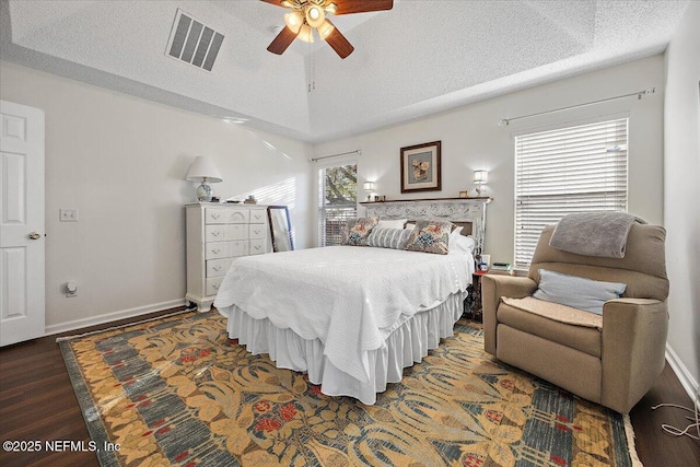 bedroom with ceiling fan, a tray ceiling, dark wood-type flooring, lofted ceiling, and a textured ceiling