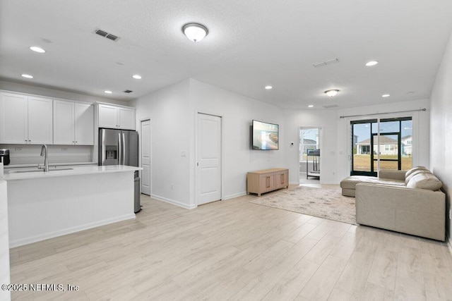 unfurnished living room featuring a textured ceiling, sink, and light hardwood / wood-style flooring