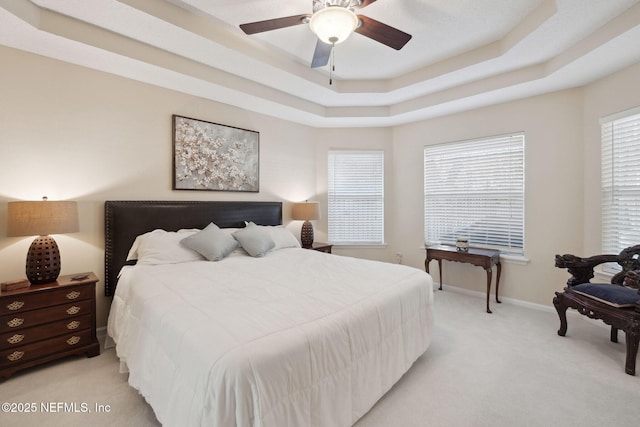 carpeted bedroom featuring a tray ceiling, multiple windows, and ceiling fan