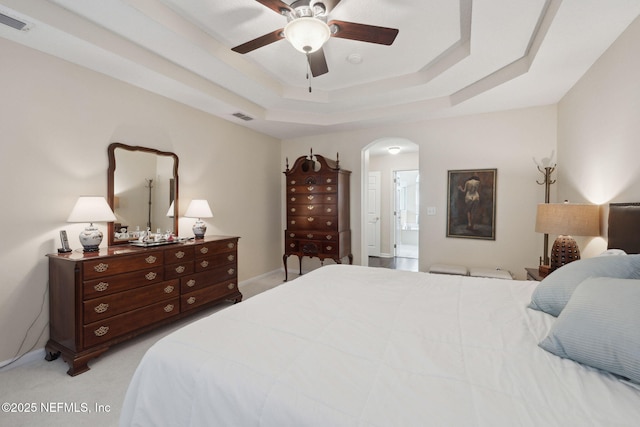 bedroom featuring a tray ceiling, ceiling fan, ensuite bathroom, and light colored carpet