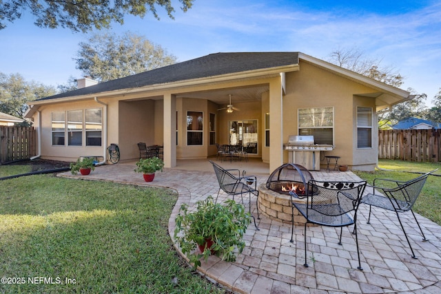 rear view of house featuring a fire pit, ceiling fan, a patio area, and a lawn