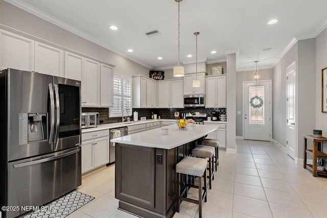 kitchen featuring appliances with stainless steel finishes, a kitchen breakfast bar, light tile patterned floors, a kitchen island, and hanging light fixtures