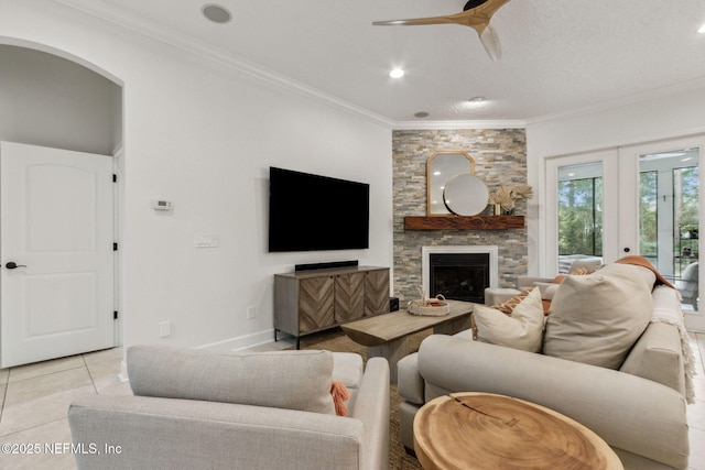 living room featuring ceiling fan, french doors, crown molding, a fireplace, and light tile patterned floors