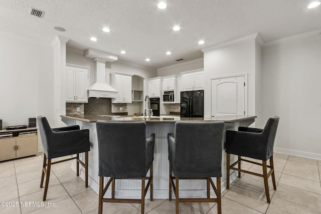 kitchen with black appliances, light tile patterned floors, custom range hood, a kitchen bar, and white cabinetry