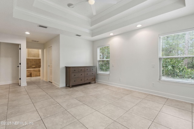 tiled empty room with a raised ceiling, ceiling fan, and ornamental molding