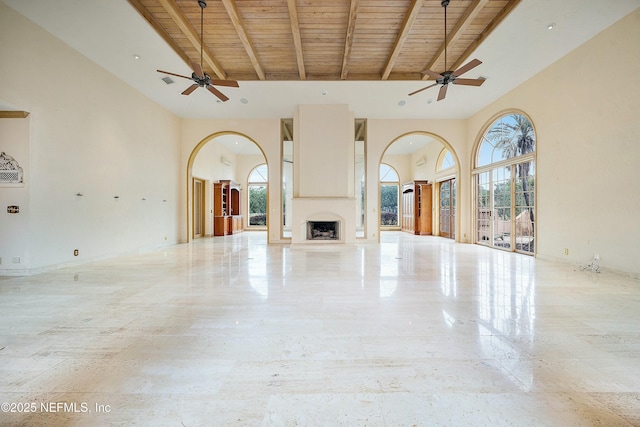 unfurnished living room featuring beamed ceiling, a high ceiling, ceiling fan, and wood ceiling