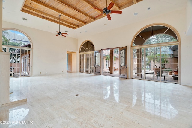 interior space with a towering ceiling, a wealth of natural light, ceiling fan, beam ceiling, and wooden ceiling