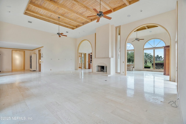 unfurnished living room featuring beam ceiling, ceiling fan, wooden ceiling, and a high ceiling