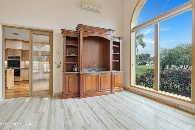 bar featuring sink, black double oven, a wall unit AC, and light hardwood / wood-style flooring