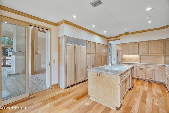 kitchen with light wood-type flooring, a kitchen island with sink, sink, paneled built in refrigerator, and light brown cabinets