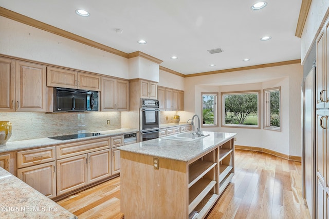 kitchen featuring light wood-type flooring, crown molding, sink, black appliances, and a center island with sink