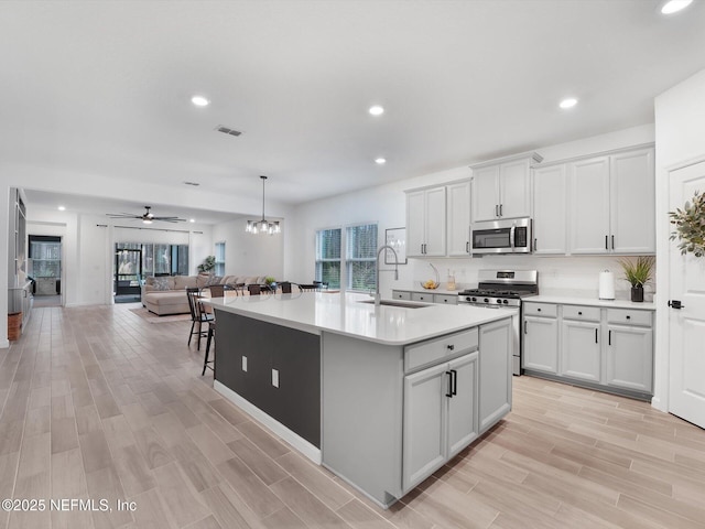 kitchen with an island with sink, stainless steel appliances, pendant lighting, ceiling fan with notable chandelier, and sink