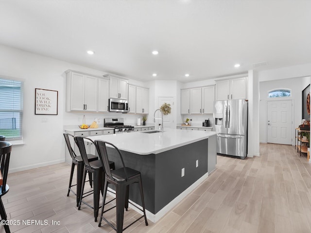 kitchen featuring white cabinetry, stainless steel appliances, a kitchen breakfast bar, a kitchen island with sink, and light wood-type flooring