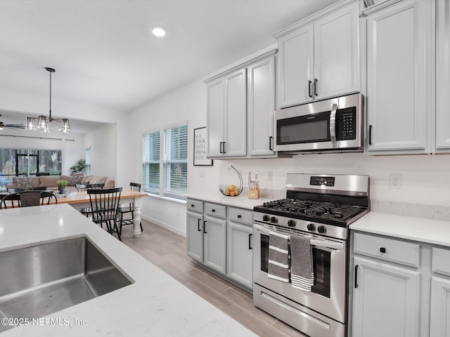 kitchen with ceiling fan, appliances with stainless steel finishes, light wood-type flooring, pendant lighting, and light stone counters