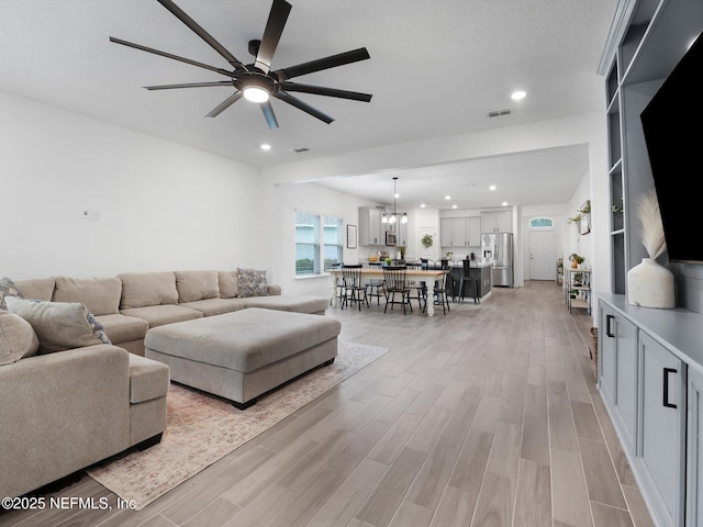 living room with light wood-type flooring and ceiling fan with notable chandelier