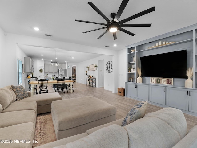 living room with ceiling fan with notable chandelier, built in shelves, and light wood-type flooring