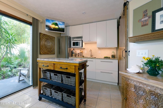 kitchen featuring white cabinetry, freestanding refrigerator, light countertops, and white microwave